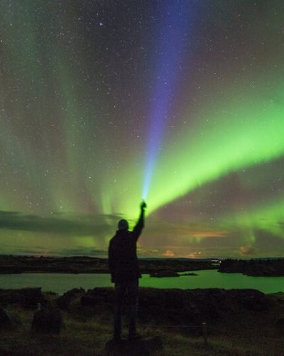 Person with flashlight, Northern Lights over Lake Mývatn in the background.