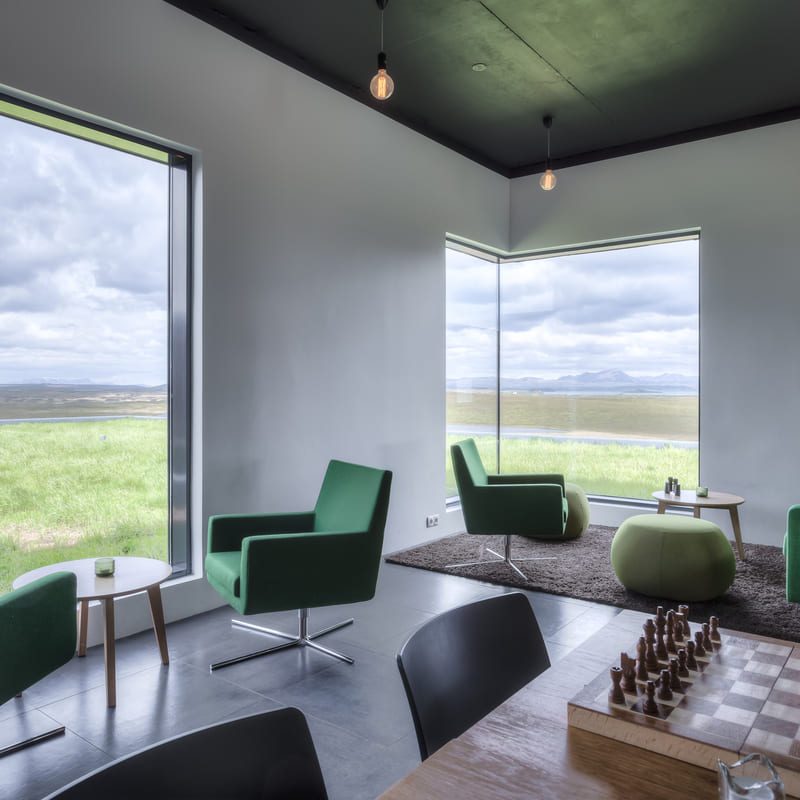 Cozy lounge area with green chairs, chess set, and panoramic view of Lake Myvatn at Hotel Laxa.