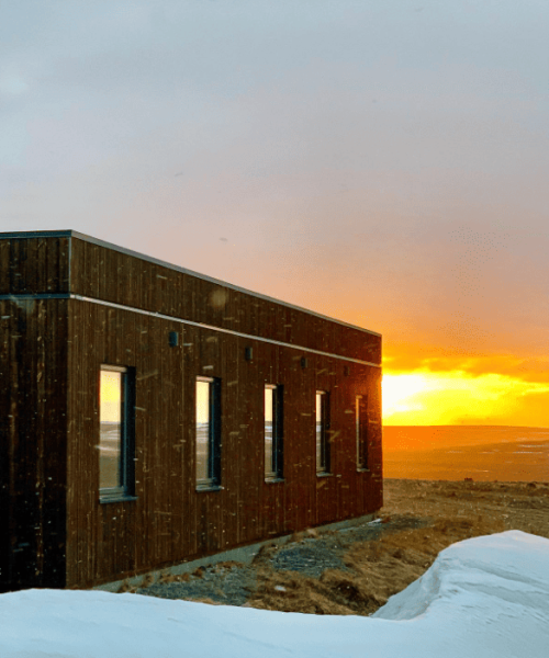 Beautiful sunset behind Hotel Laxa with snow falling and a snowy foreground, creating a peaceful winter scene in North Iceland.