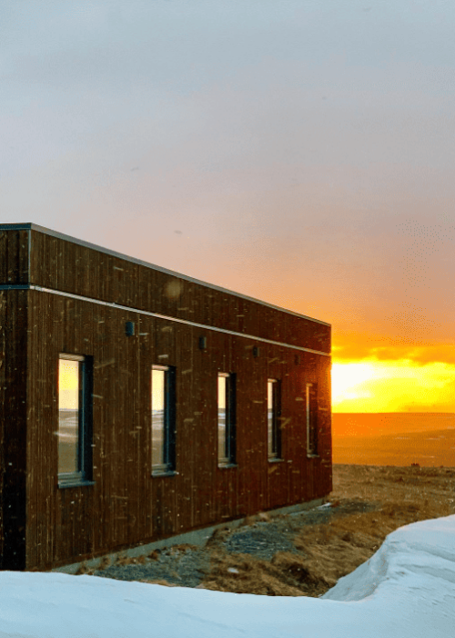 Beautiful sunset behind Hotel Laxa with snow falling and a snowy foreground, creating a peaceful winter scene in North Iceland.